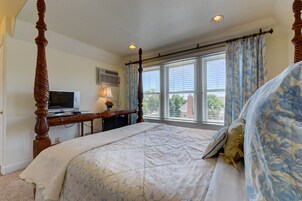 A bedroom with a four-poster bed, a desk with a computer, and a window with curtains.