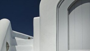 A white staircase leading to a door with a decorative metal emblem. - Avista Suites (Santorini)