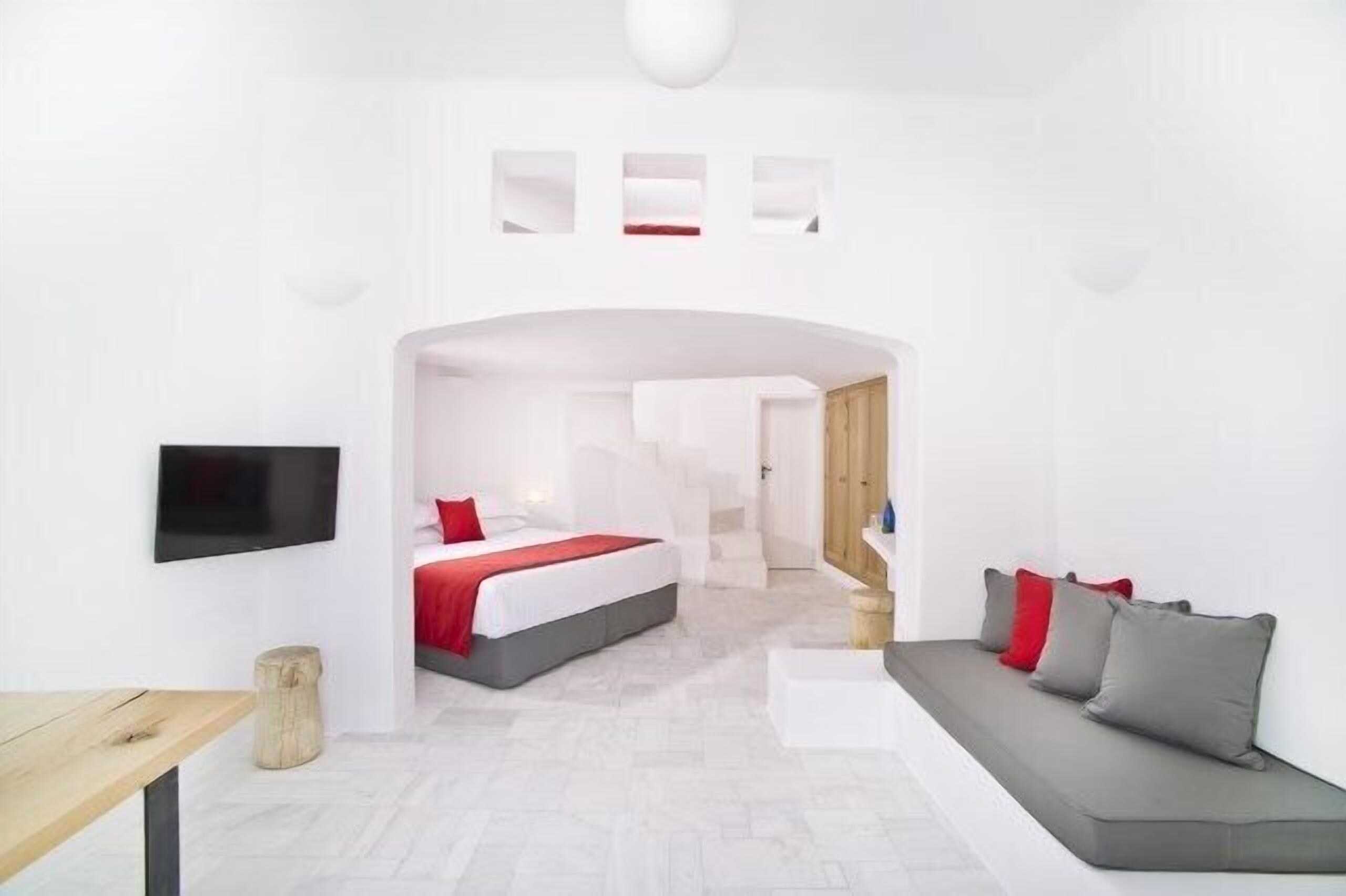 A modern hotel room with a bed, a sofa, a TV, and a small table.