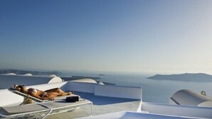 A couple relaxing on a sun lounger with a view of the sea and islands. - Avista Suites (Santorini)