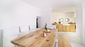 A modern kitchen with wooden cabinets, a white countertop, and a dining area with a wooden table. - Avista Suites (Santorini)