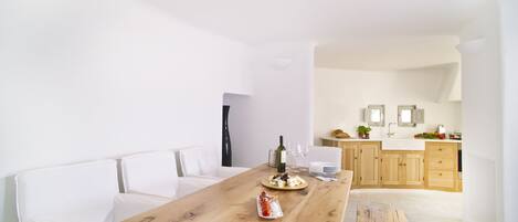 A modern kitchen with wooden cabinets, a white countertop, and a dining area with a wooden table.