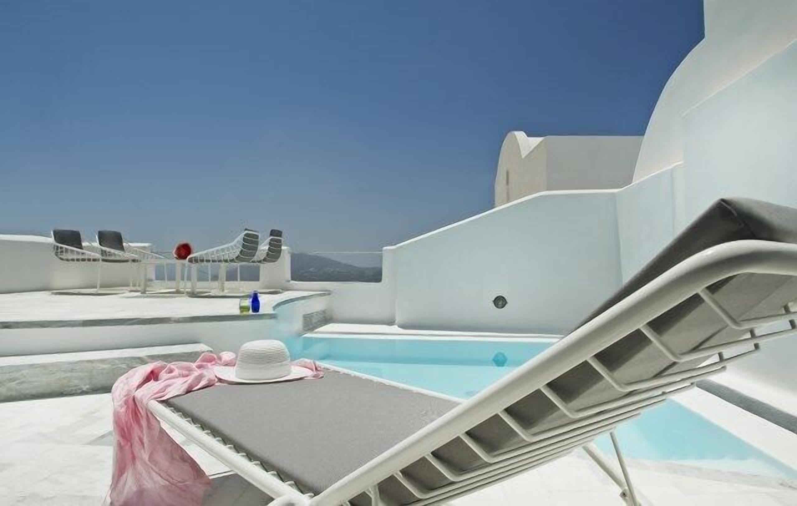 A rooftop pool area with lounge chairs and a table, clear skies, and a view of the sea.