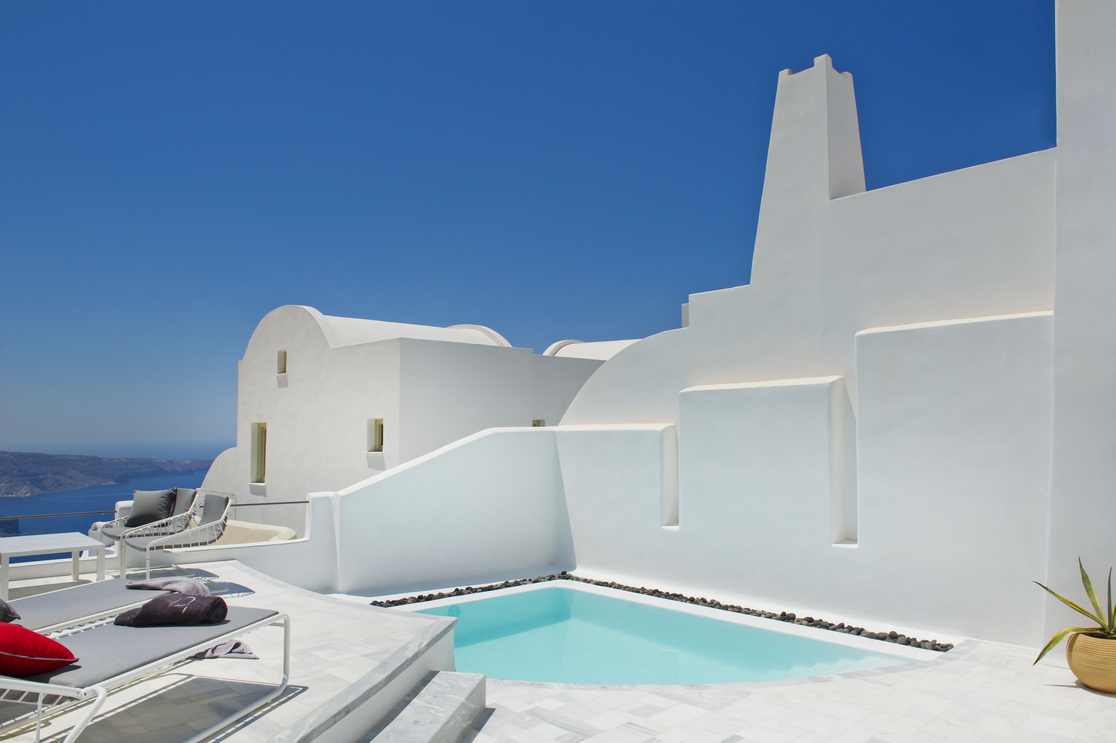 Un bâtiment moderne de couleur blanche, doté d’une piscine et de chaises longues.