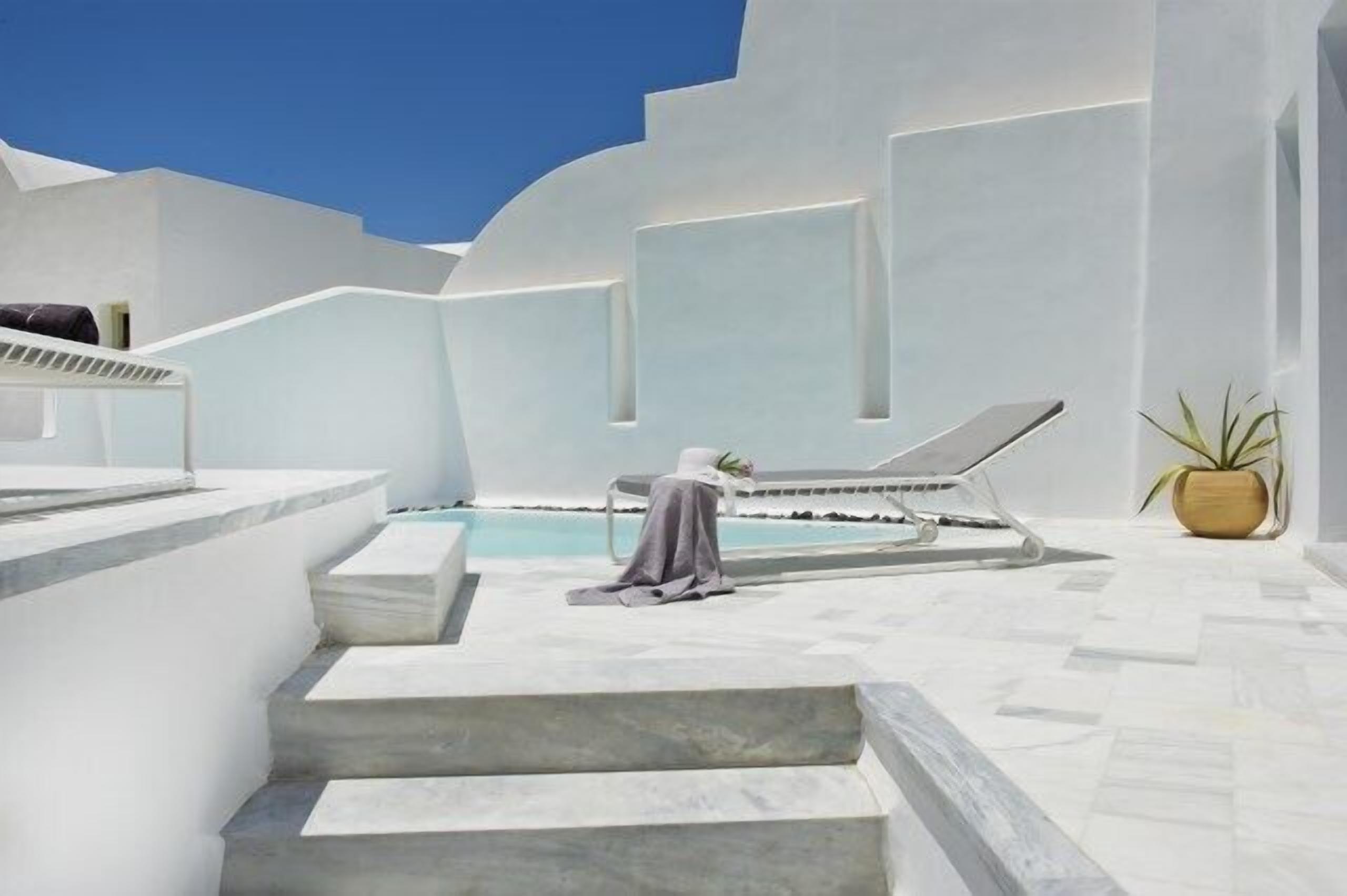 A modern outdoor pool area with a clear blue sky, white walls, and a single lounge chair.