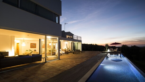 Ein modernes Haus mit Schwimmbad, Glastüren zu einem Wohnbereich und einem Balkon mit Sitzgelegenheit.
