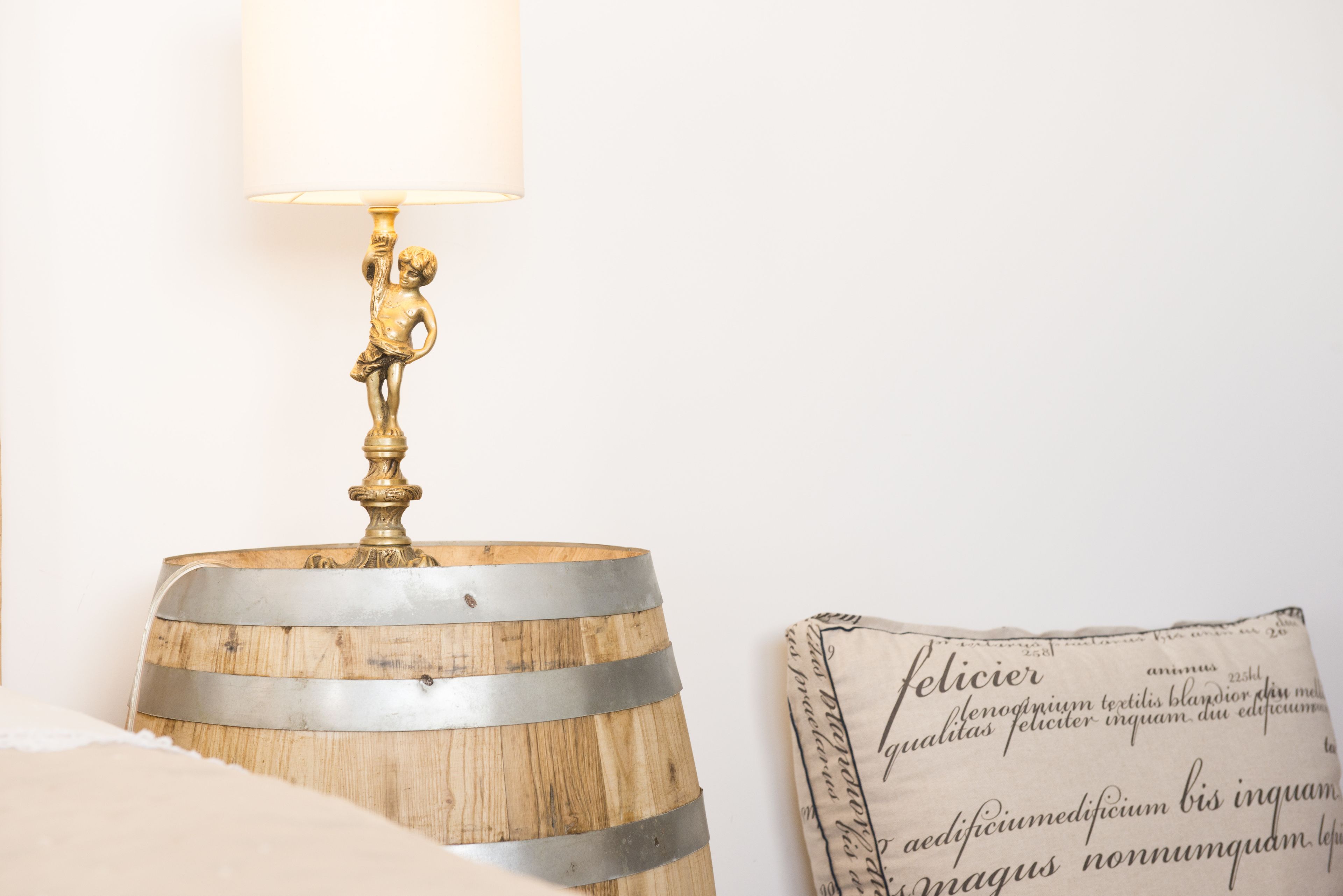 A lamp with a decorative base and a lit shade, placed on a wooden barrel.