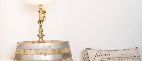 A lamp with a decorative base and a lit shade, placed on a wooden barrel.