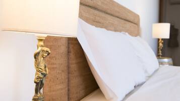 A bed with a wooden headboard, white bedding, and a brass lamp with a statue base.