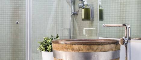 Een badkamer met een wasbak in de vorm van een houten vat, een douchecabine van glas en een wit aanrecht.