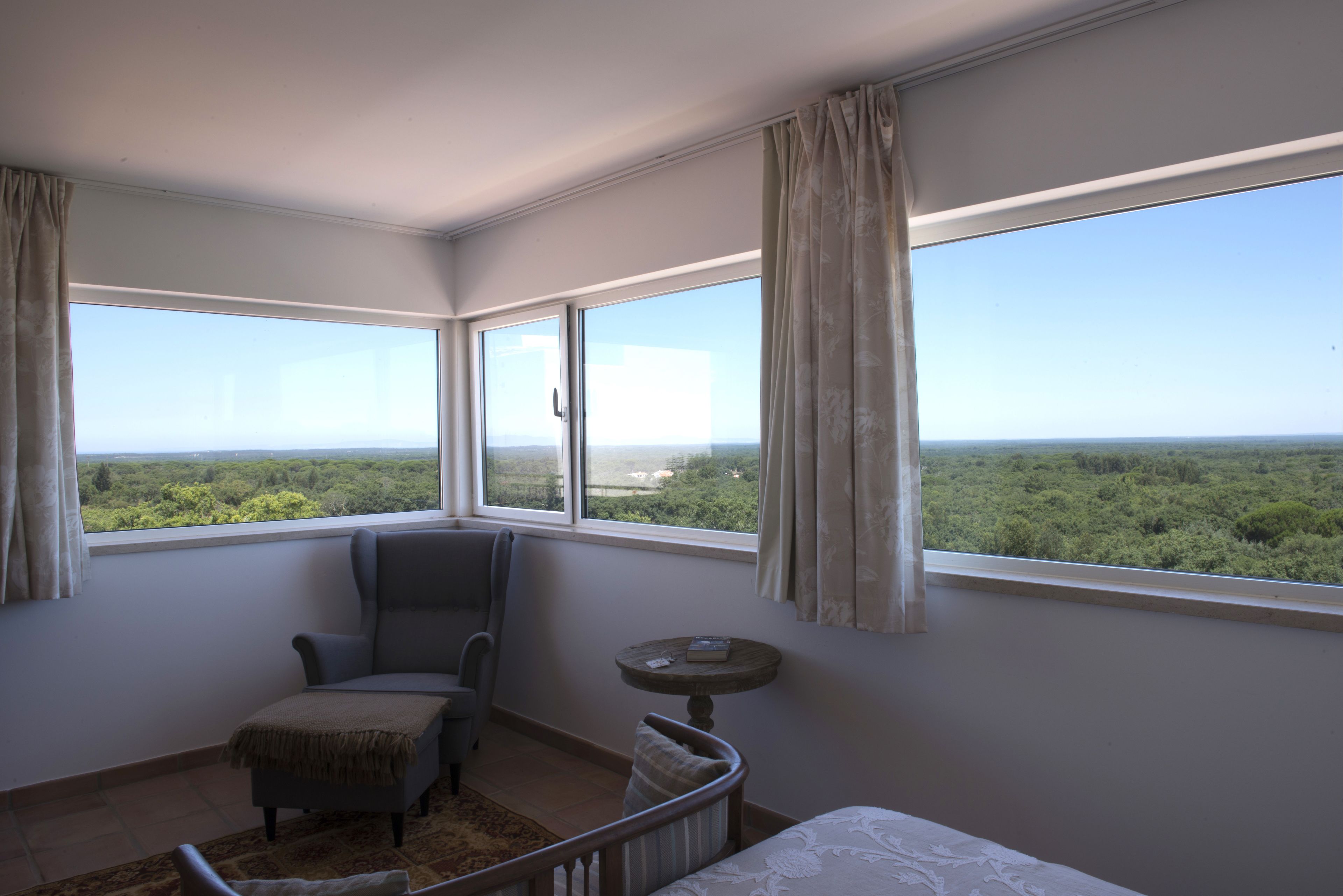 A room with a large window, a chair, a small table, and a bed.