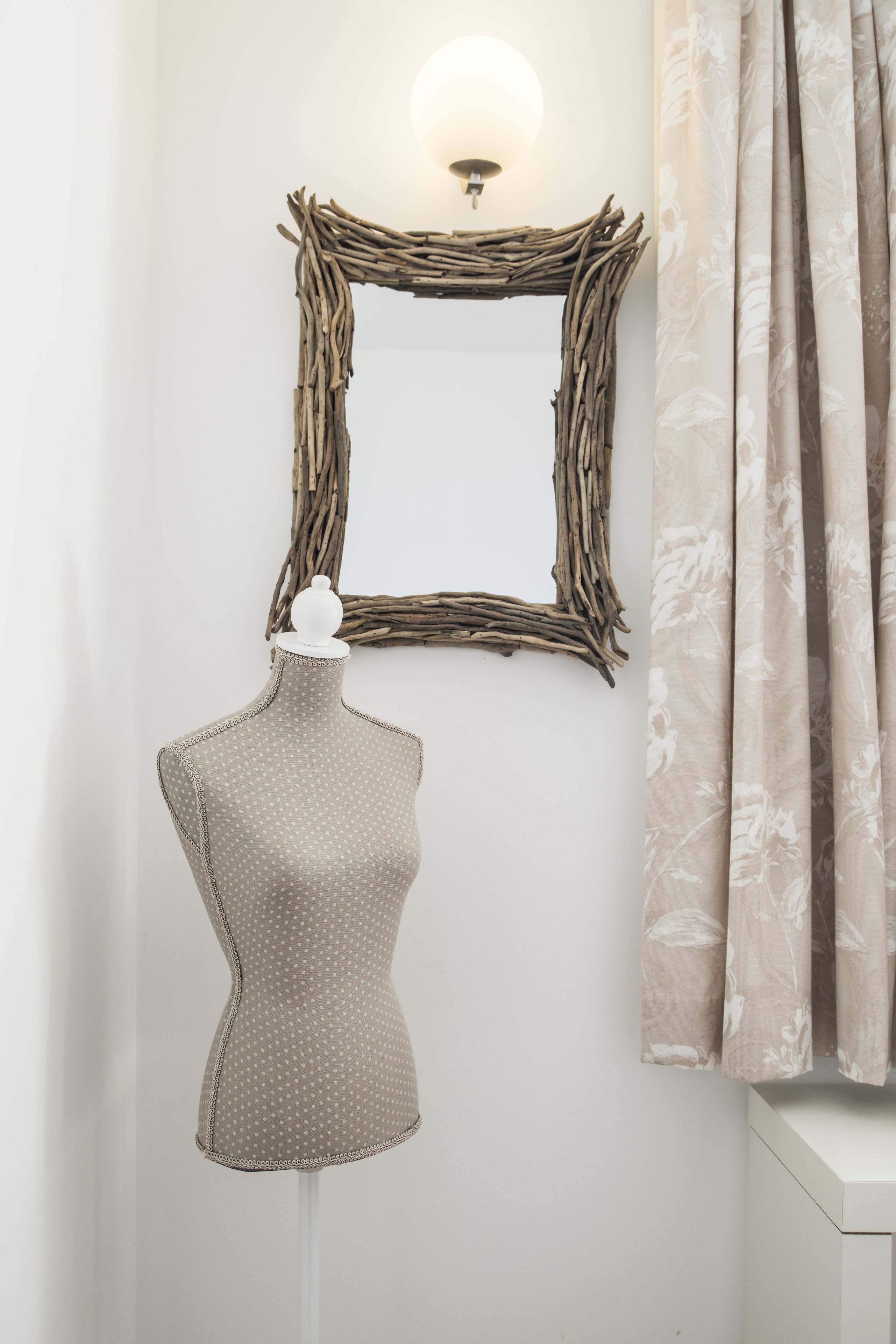 A mannequin in a room with a mirror, a wall-mounted light, and curtains.