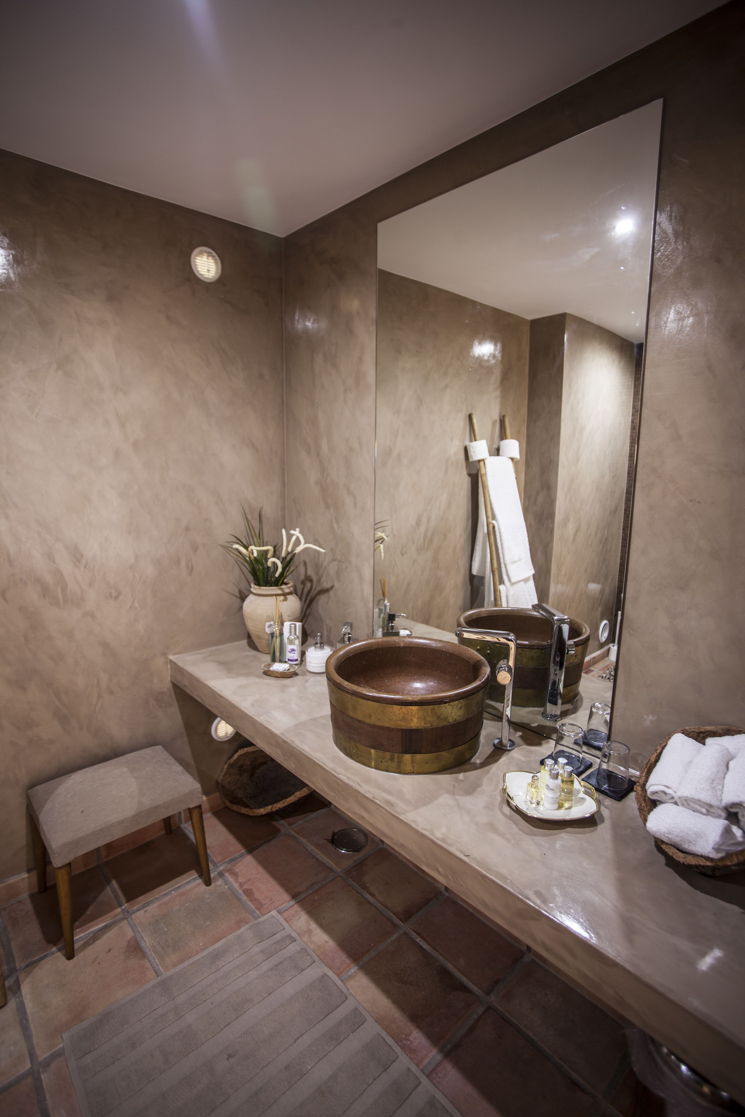 A bathroom with a large mirror, a wooden basin, a small stool, and a potted plant.