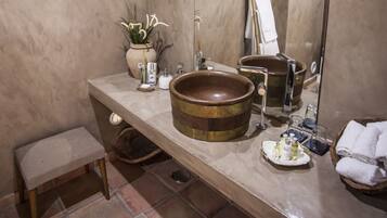 A bathroom with a large mirror, a wooden basin, a small stool, and a potted plant.
