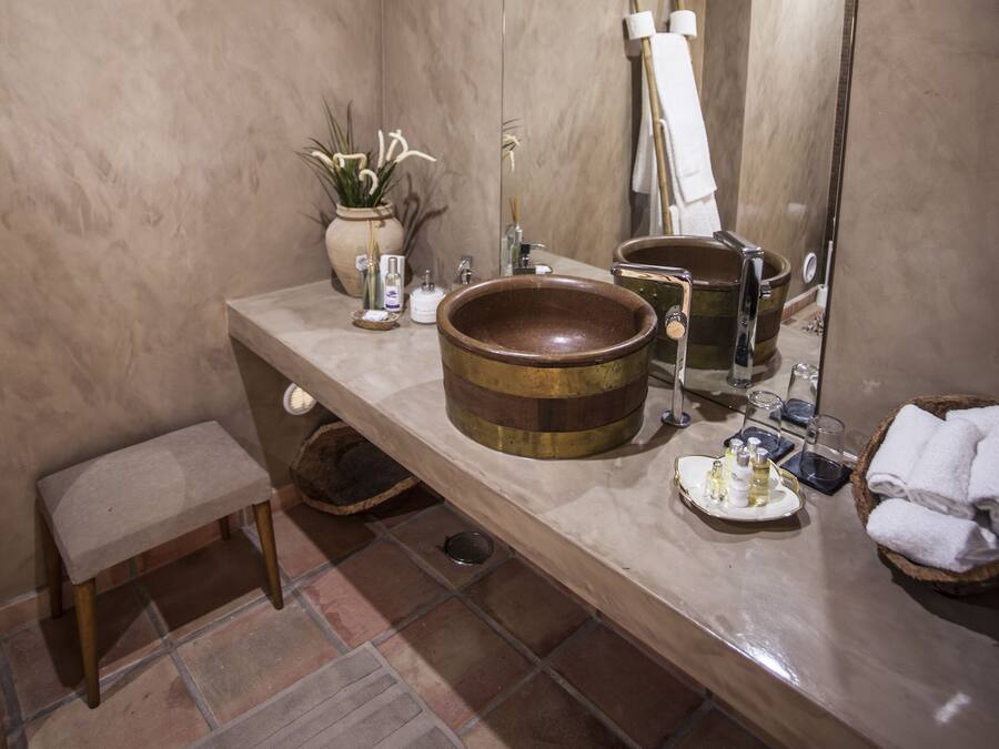 A bathroom with a large mirror, a wooden basin, a small stool, and a potted plant.