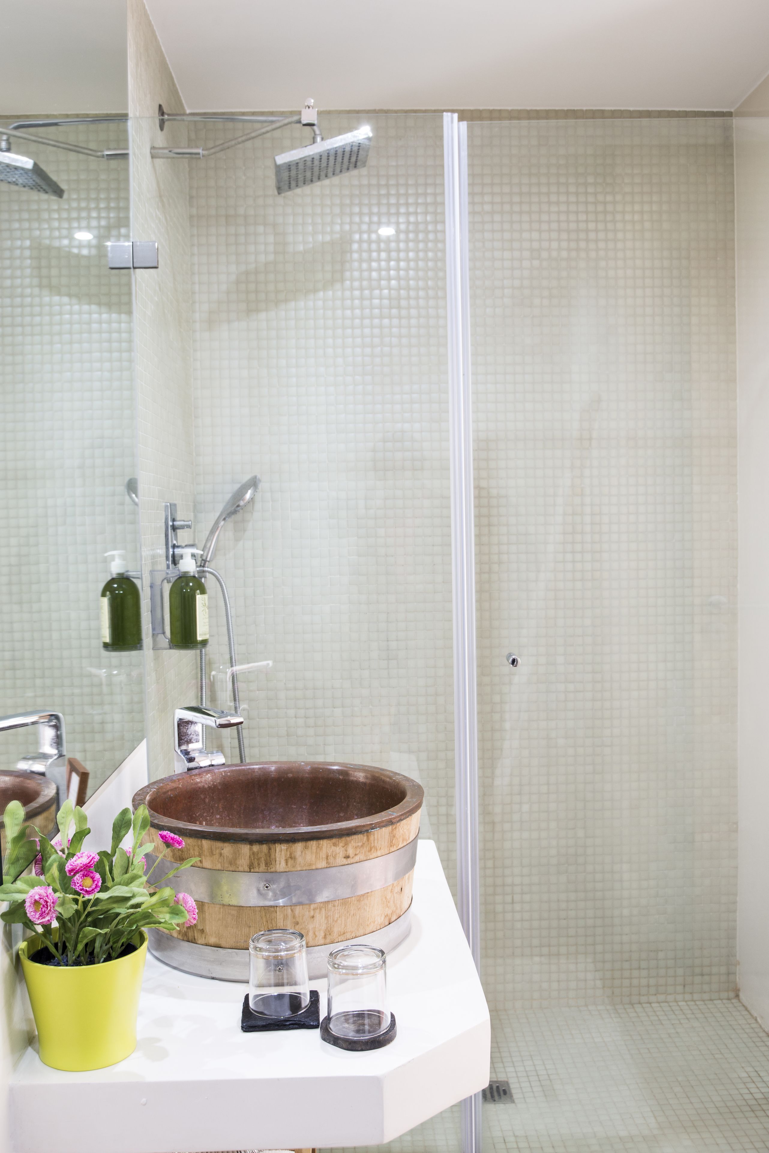 A bathroom with a wooden basin sink, a glass shower enclosure, and a yellow flower pot.