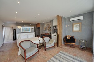 Una habitación de hotel con una cama, dos sillones, un escritorio y un equipo de aire acondicionado.