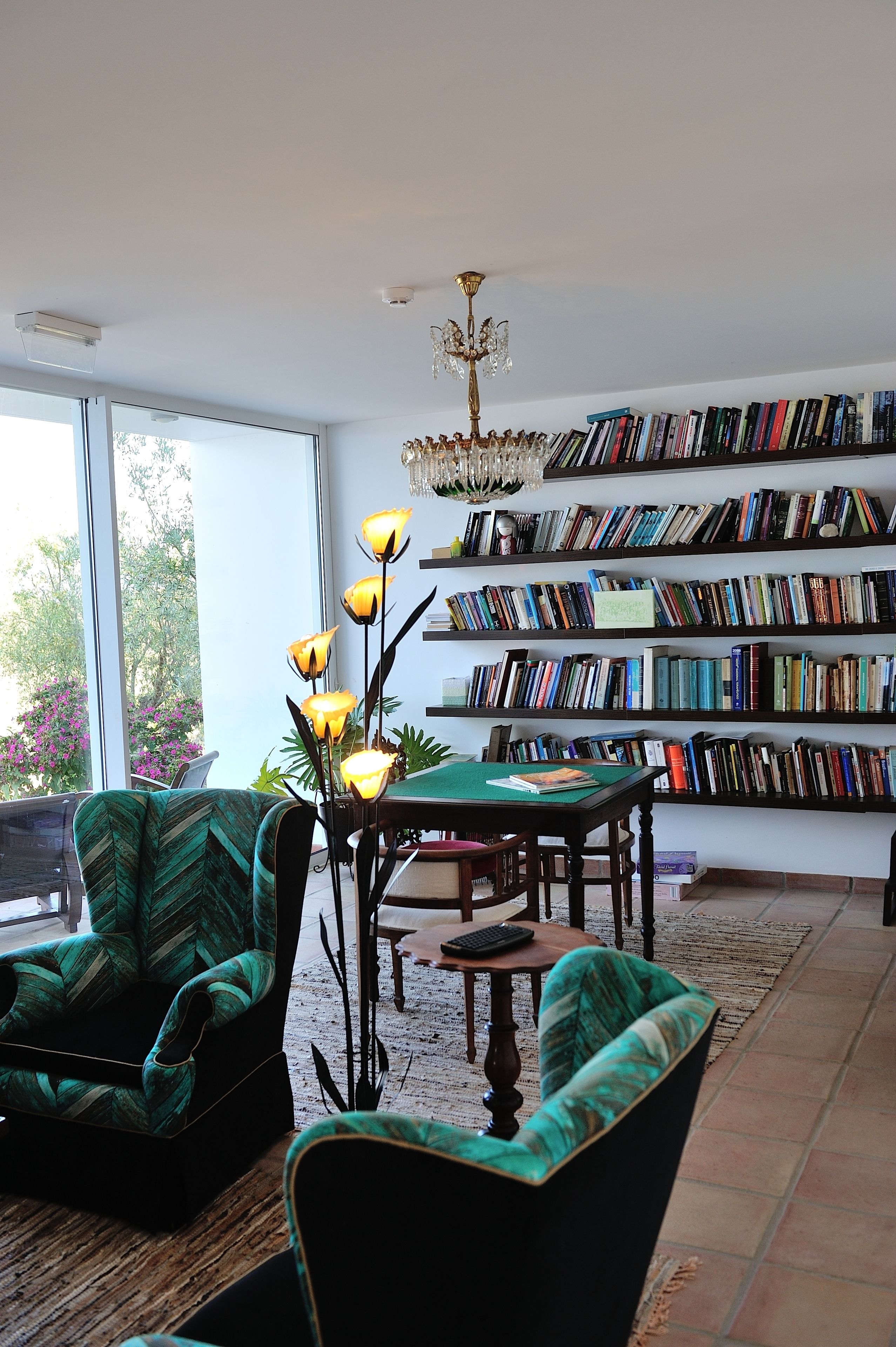 A spacious living room with a large bookshelf, a chandelier, and a view through a large window.