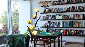 A spacious living room with a large bookshelf, a chandelier, and a view through a large window.