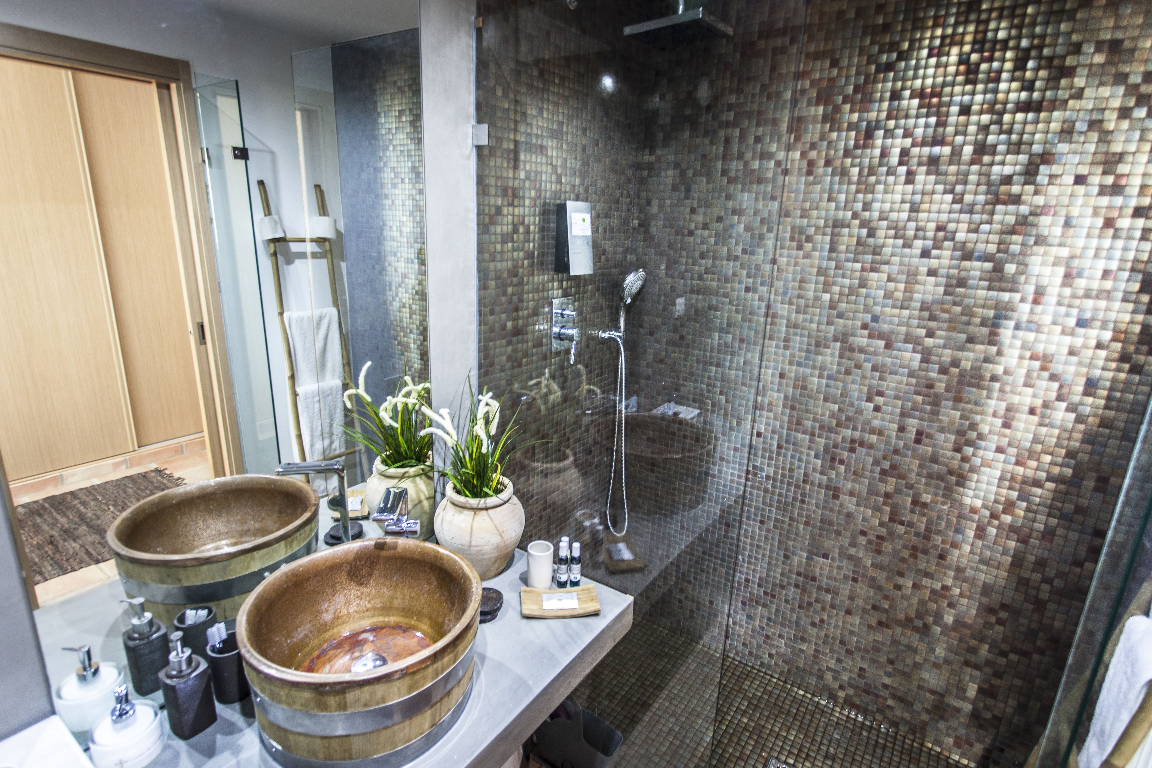 Un baño con un espejo grande, dos cuencos de madera, una ducha y una pared con azulejos.