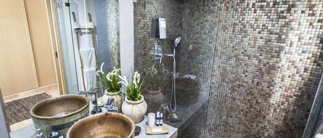 Un baño con un espejo grande, dos cuencos de madera, una ducha y una pared con azulejos.