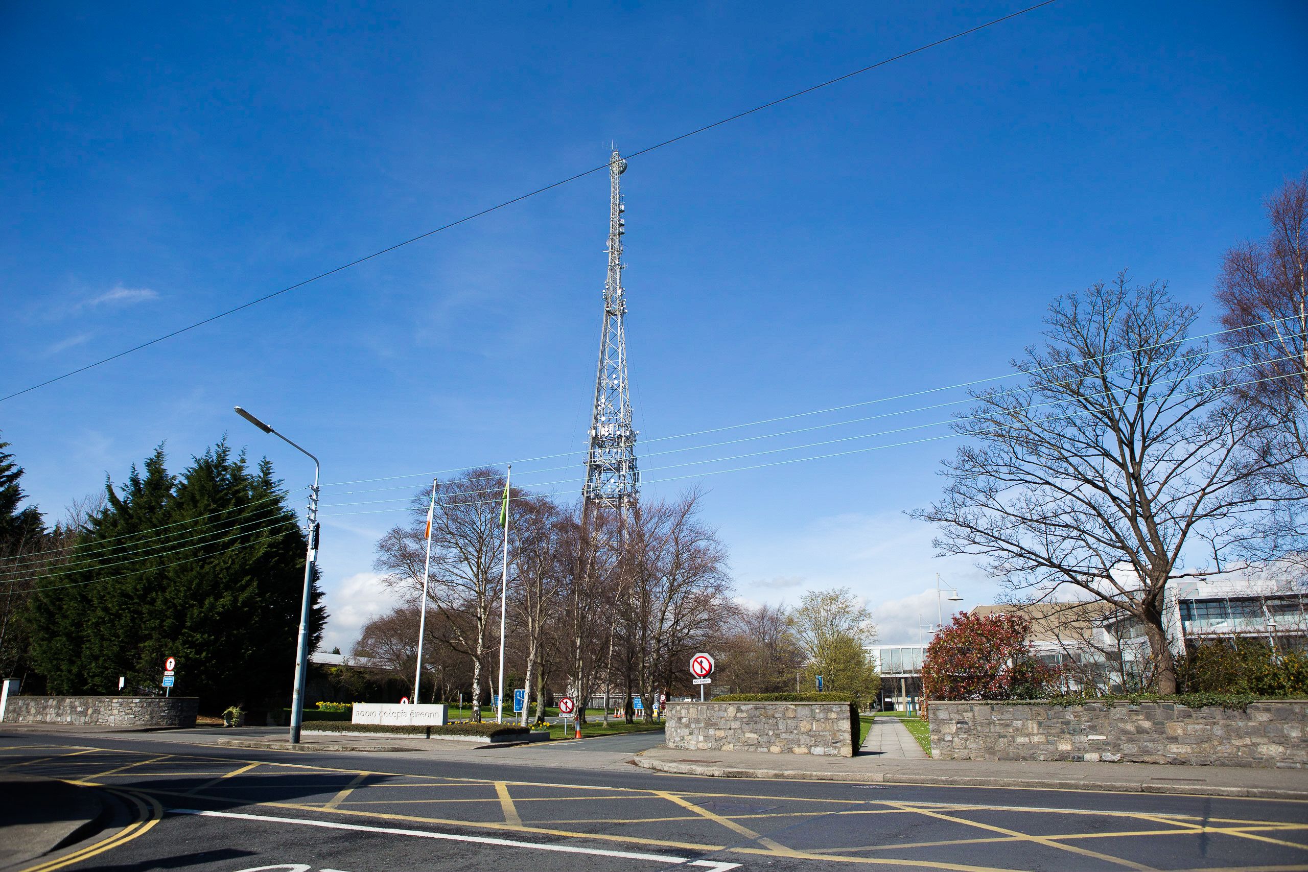 Une vue de rue avec une haute tour de communication, un rond-point et un mur de pierre orné de verdure.