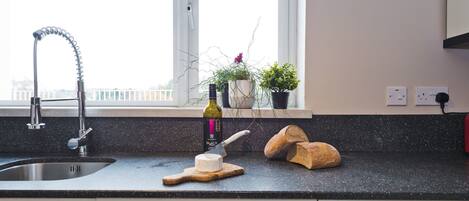 A kitchen with a stainless steel sink, a wine bottle, a cheese knife, and bread on the counter.