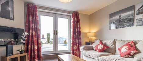 A modern living room with a sofa, a wooden coffee table, a TV on a stand, and a window with red curtains.