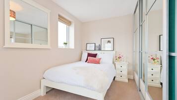 Une chambre à coucher avec un lit, des tables de chevet, un miroir et une fenêtre.