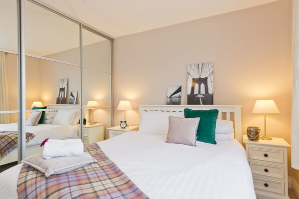 A hotel room with a large bed, a nightstand with a lamp, a mirror, and artwork on the wall. - Broc House Suites (Dublin)