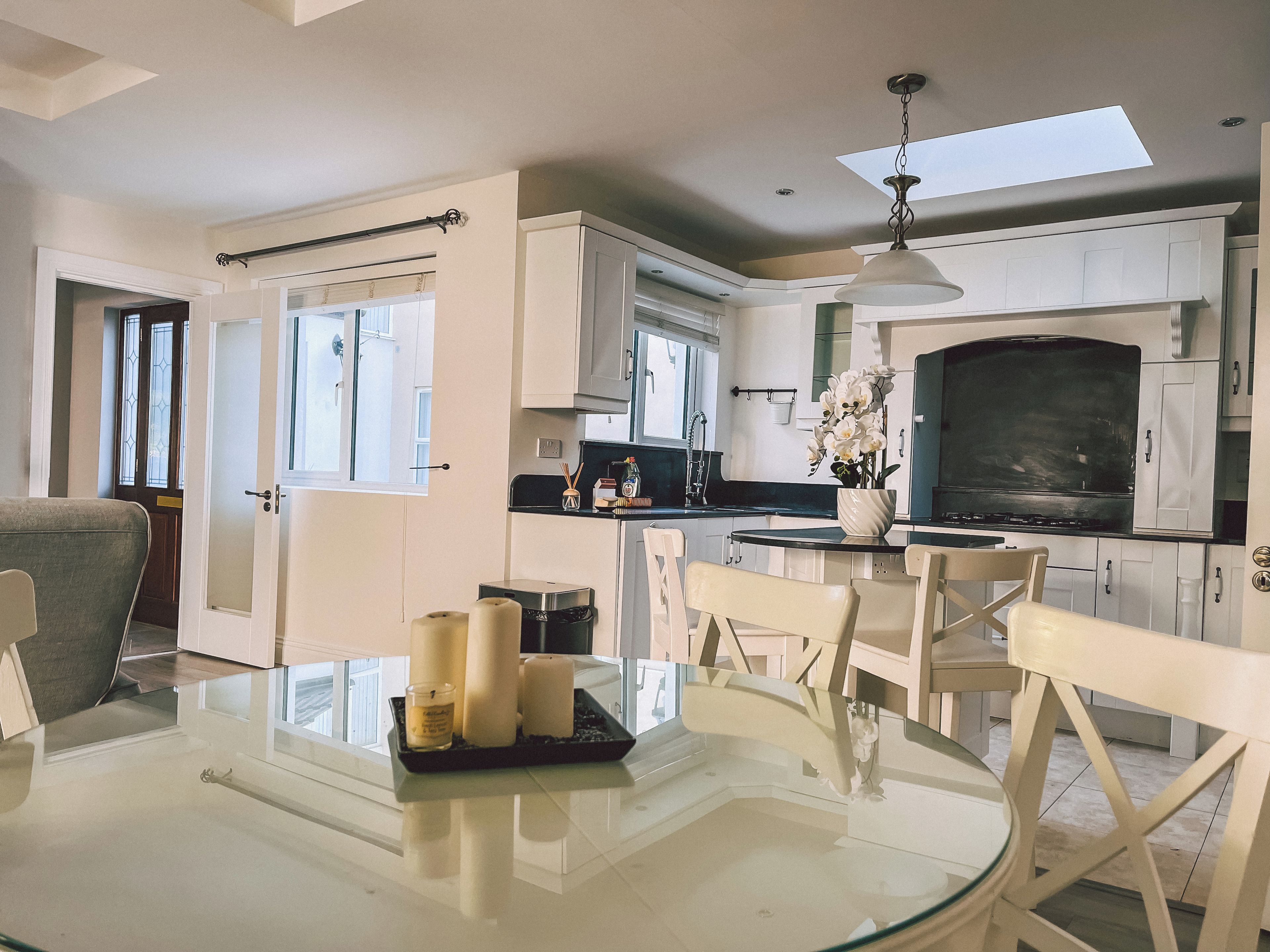 Una cocina moderna con armarios blancos, una zona de comedor con mesa de vidrio y un ventanal que proporciona luz natural.