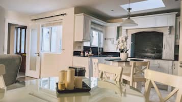 Una cocina moderna con armarios blancos, una zona de comedor con mesa de vidrio y un ventanal que proporciona luz natural.