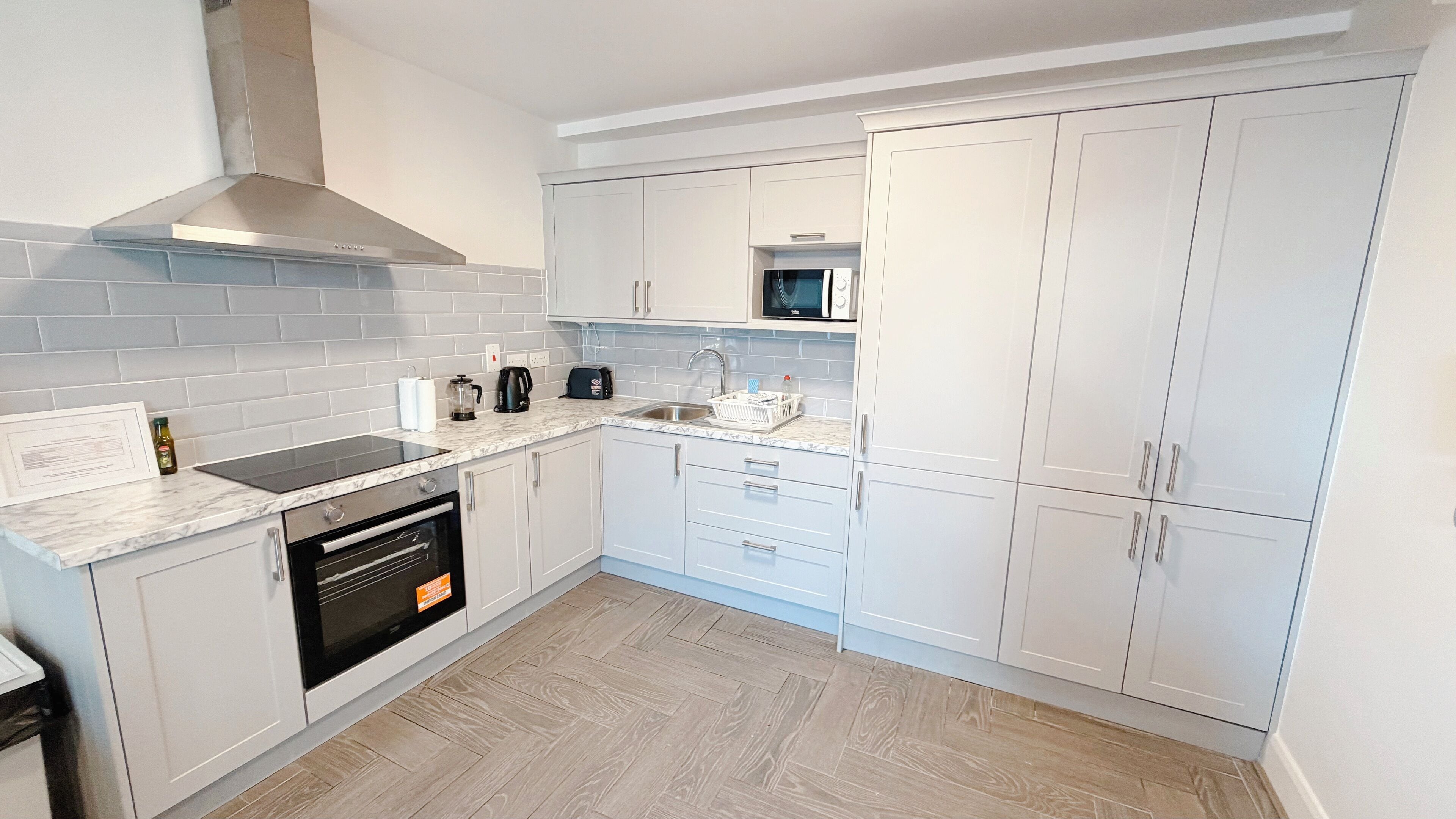 A modern kitchen with white cabinetry, a built-in oven, a microwave, and a stainless steel sink.