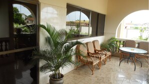A covered patio area with wicker furniture, potted plants, and large windows offering views of the surrounding area. - Sheridan Hotel (Accra)