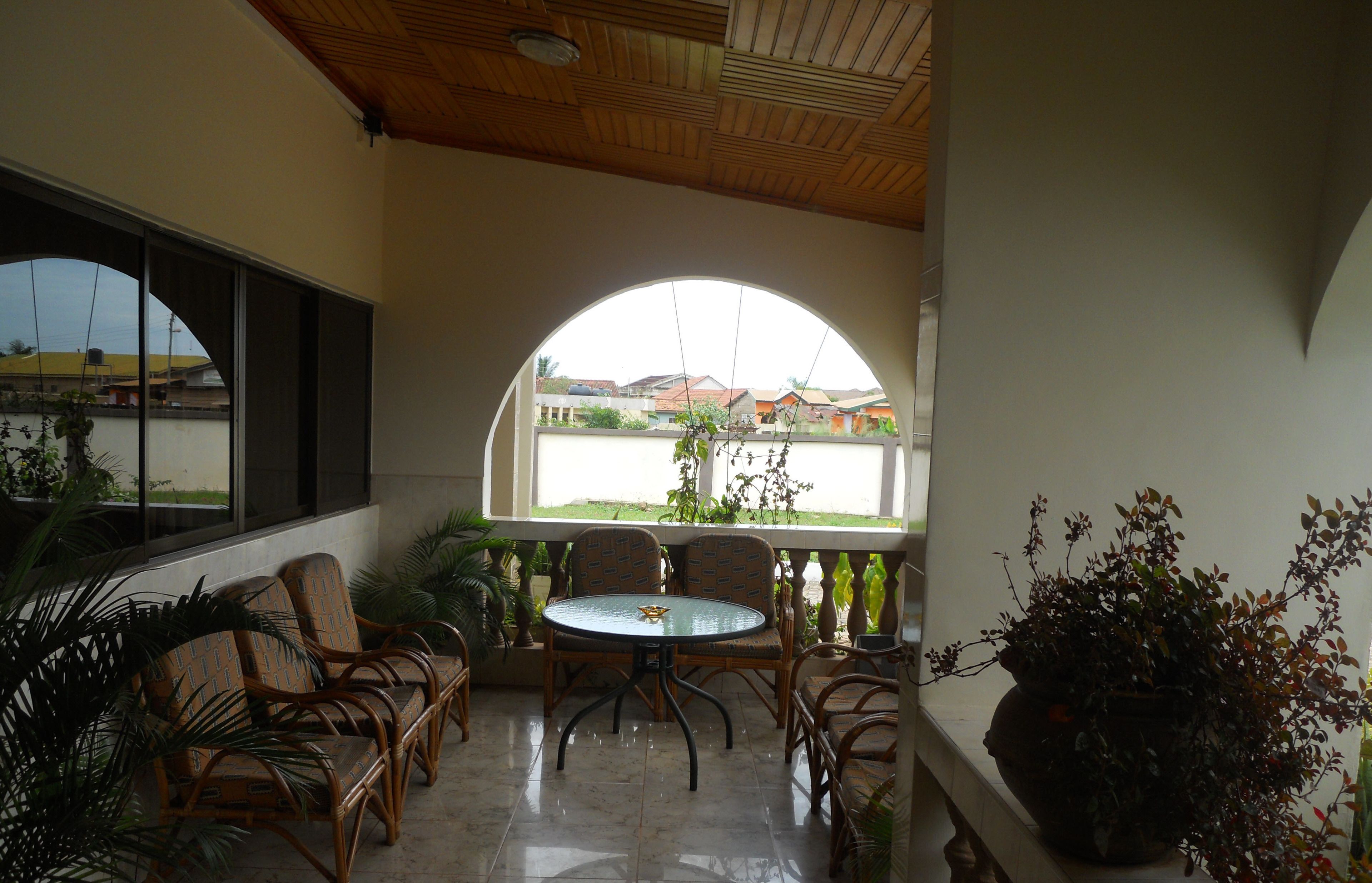 A covered patio with wicker furniture, a glass table, and potted plants.