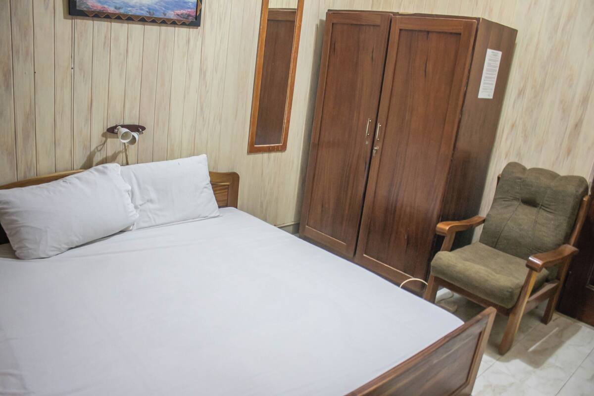 A bedroom with a bed, wooden wardrobe, and a chair.