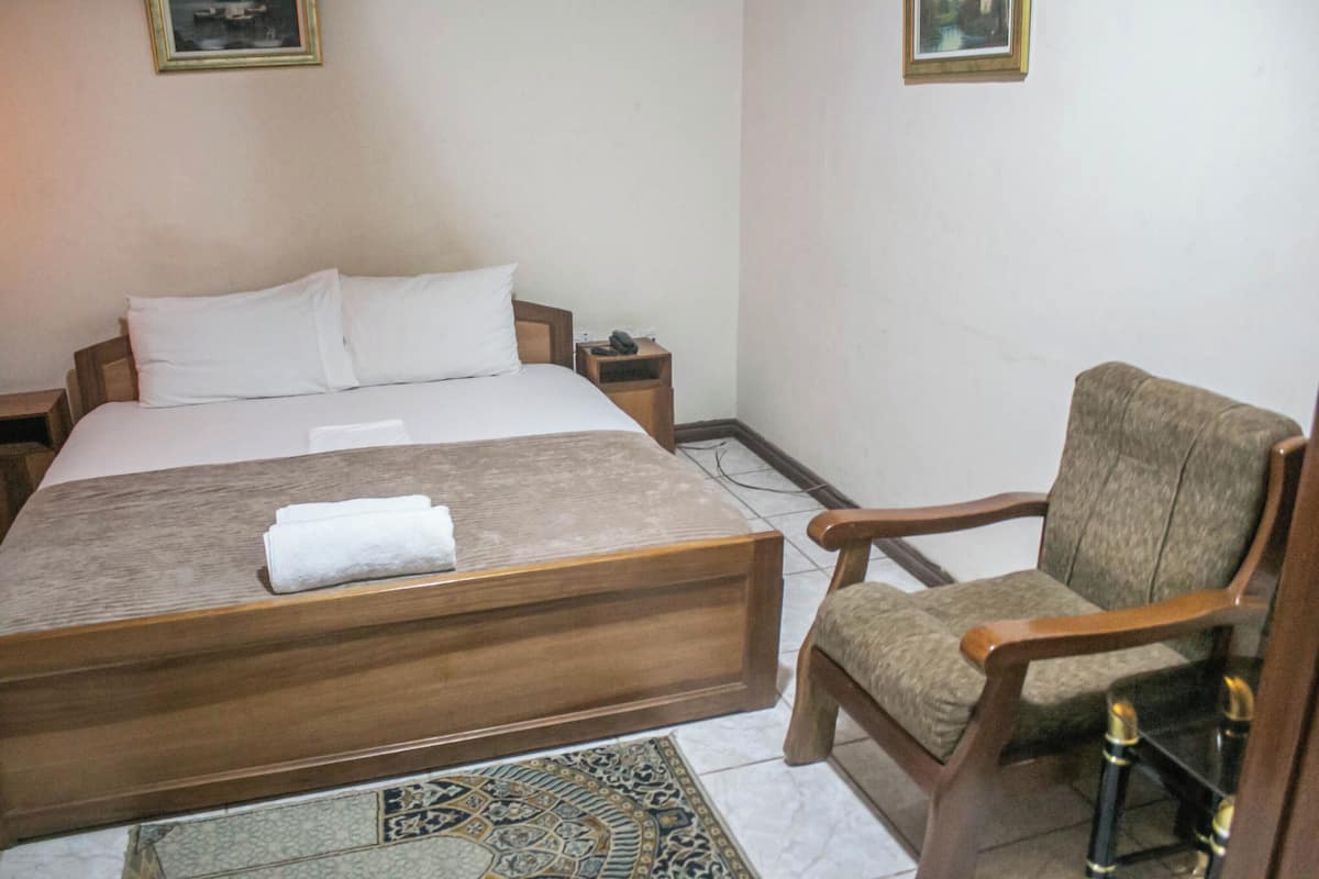 A hotel room with a large bed, a wooden nightstand, a chair, and a patterned rug.