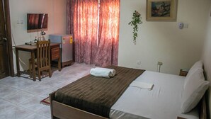 A bedroom with a bed, a desk, a chair, a TV, and a painting on the wall. - Sheridan Hotel (Accra)