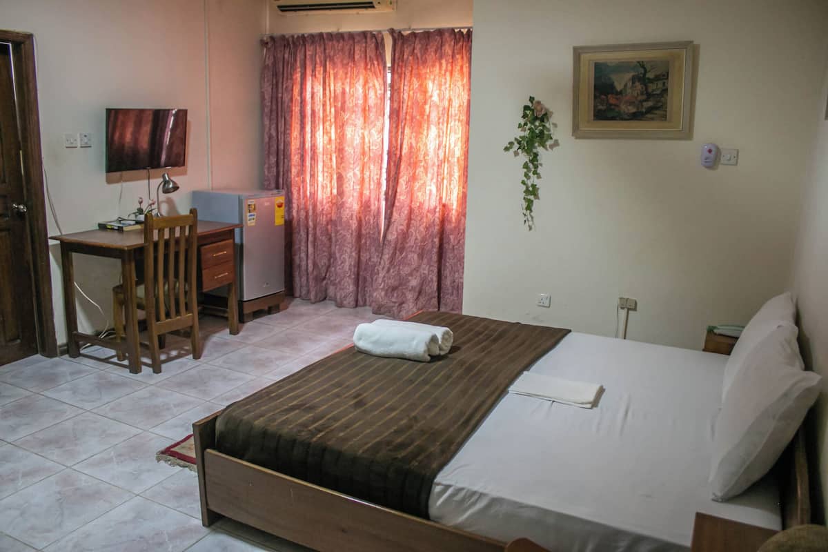 A bedroom with a bed, a desk, a chair, a TV, and a painting on the wall.