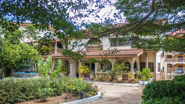 A courtyard with a fountain, potted plants, and a brick pathway leading to a building with multiple balconies and arches. - Sheridan Hotel (Accra)