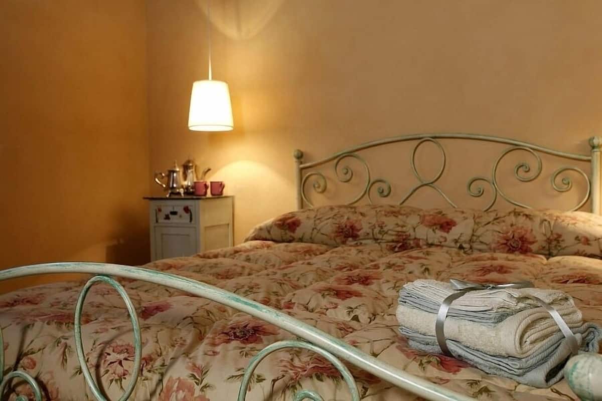 A bed with floral bedding, a metal headboard, a bedside table with a lamp, and a folded towel on the bed.