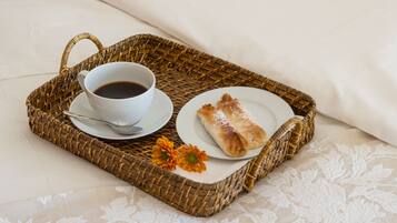 Una bandeja de mimbre con una taza de café, un plato con un pastel y una flor sobre una cama con una colcha blanca.