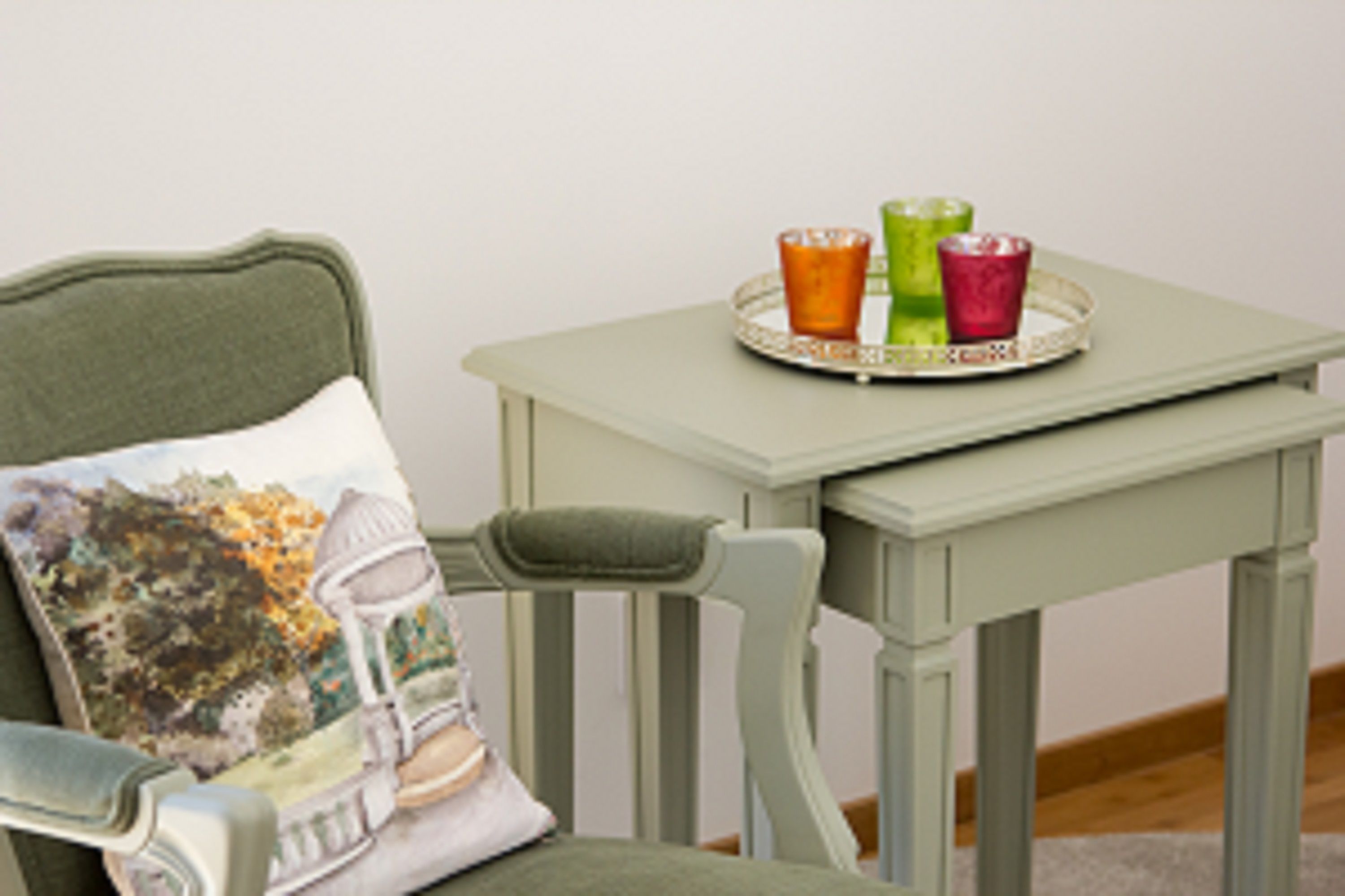 A chair with a cushion featuring a landscape design, a small table with a tray holding three glasses, and a plain wall in the background.