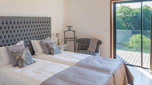 A bedroom with a large bed, a nightstand, a chair, and a view of greenery outside. - Quinta do Fontelo (Vouzela)