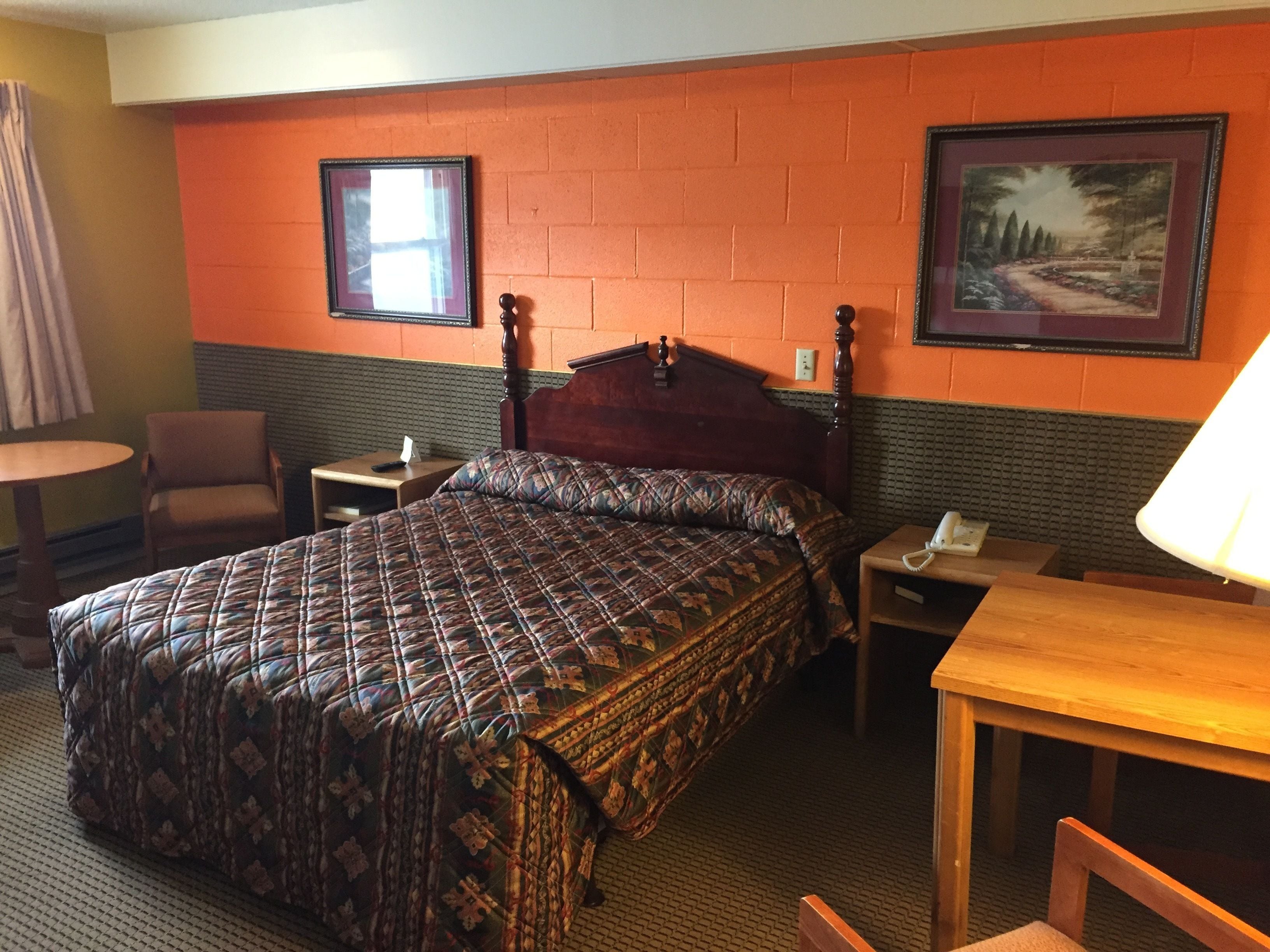 A hotel room with a large bed, a chair, a table, a nightstand, and a lamp.