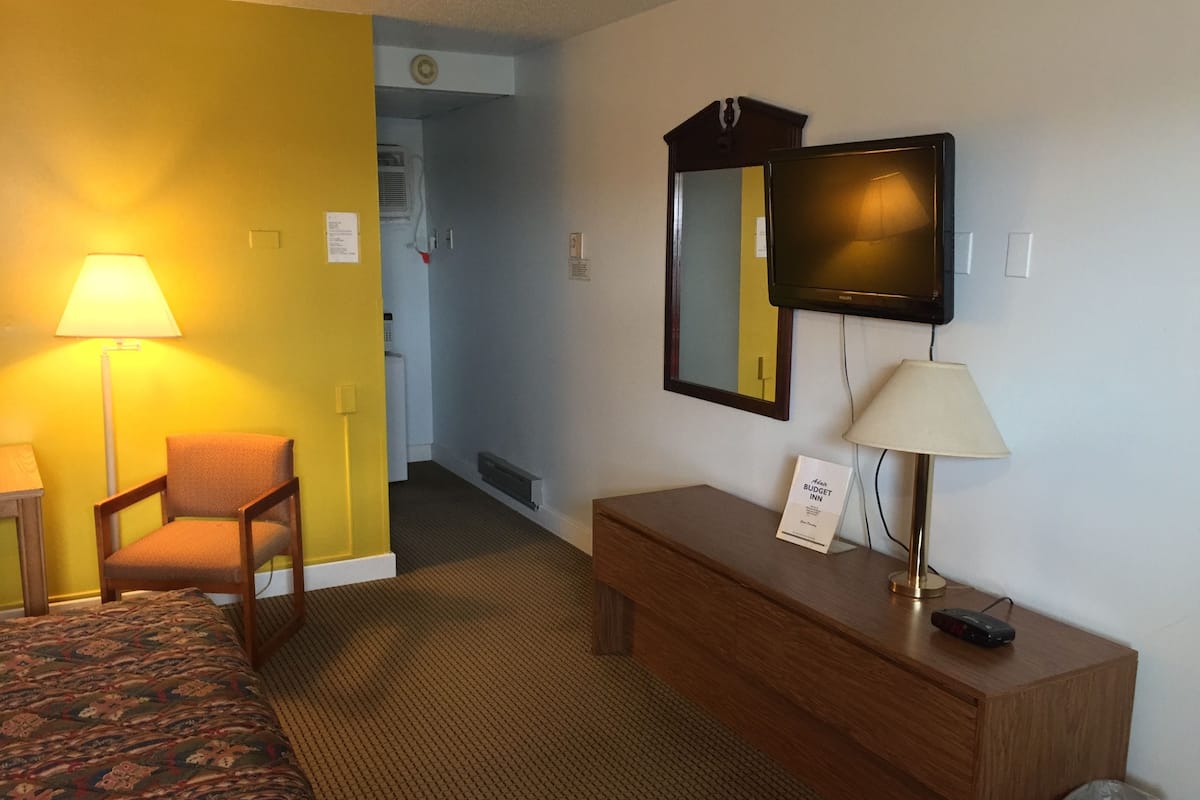 A hotel room with a bed, a chair, a desk, a television, and a lamp.
