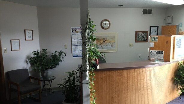 A reception area with a wooden desk, potted plants, framed artwork, and a wall calendar. - Adair Budget Inn (Adair)
