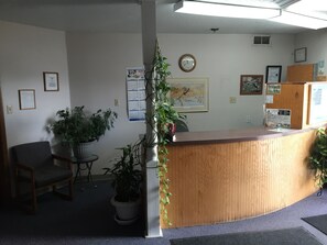 A reception area with a wooden desk, potted plants, framed artwork, and a wall calendar.