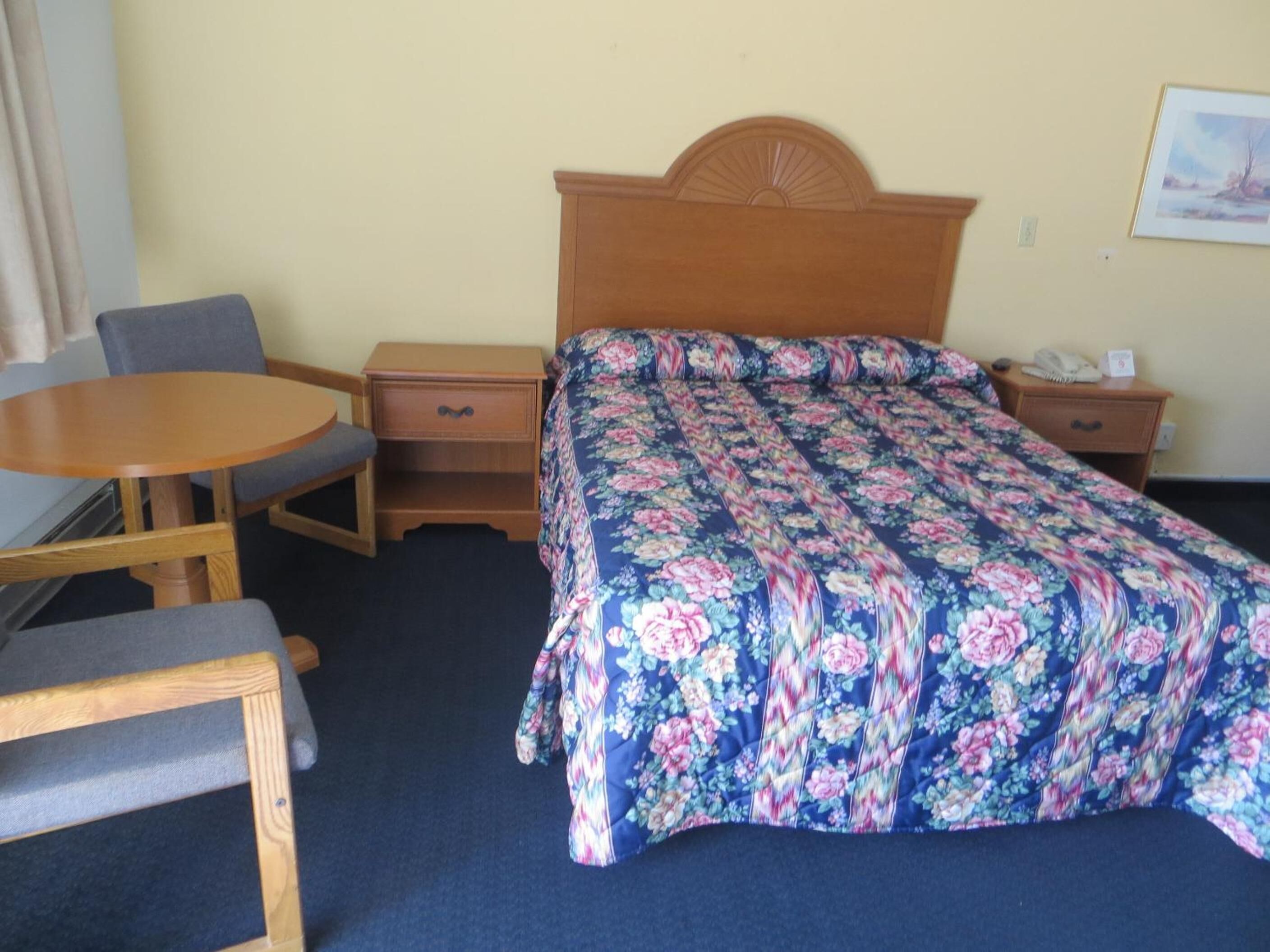 Une chambre d’hôtel comprenant un lit, une table de chevet en bois, un bureau avec une chaise et une petite table ronde.