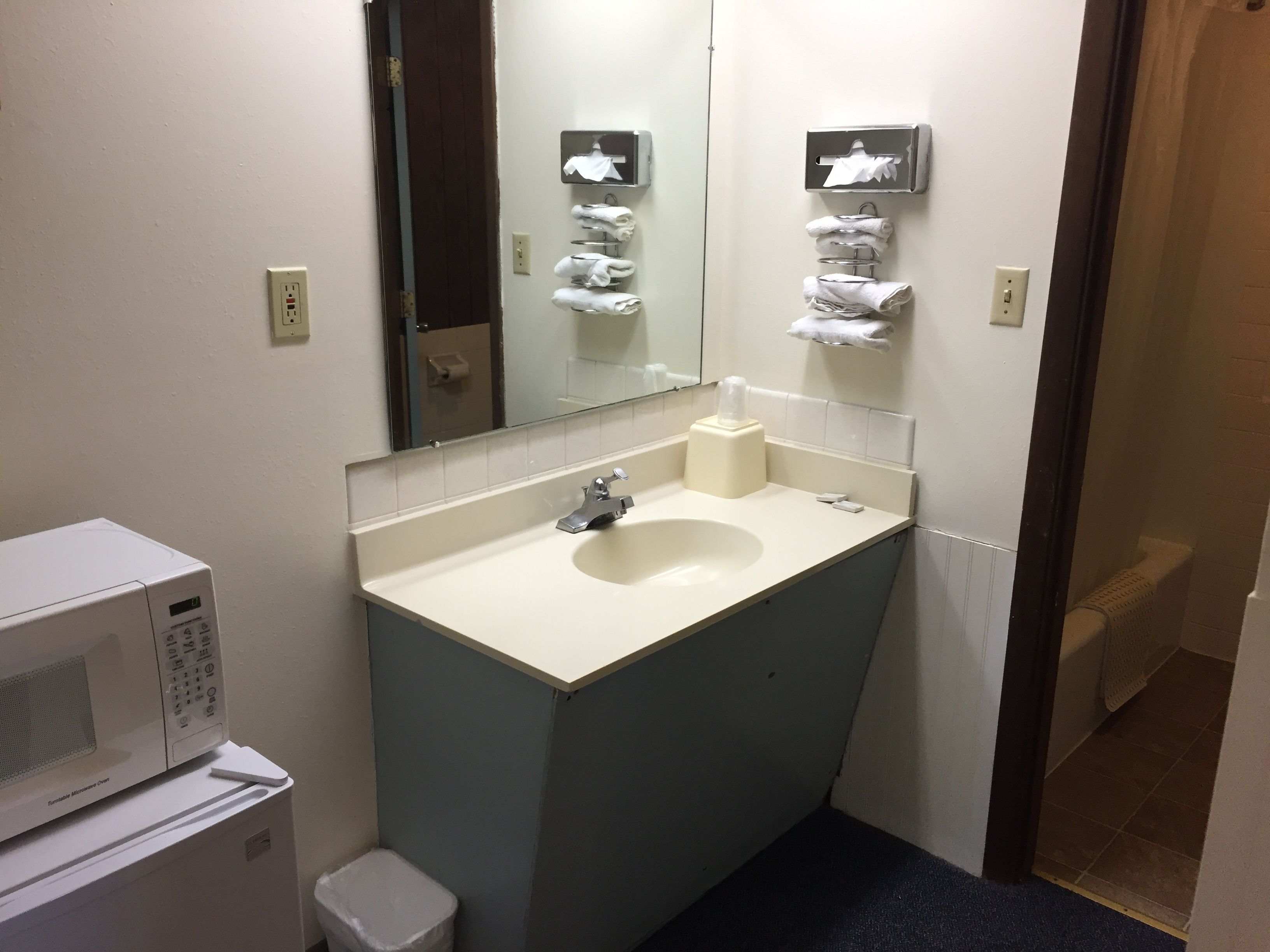 A small bathroom with a sink, mirror, towel rack, and a microwave.